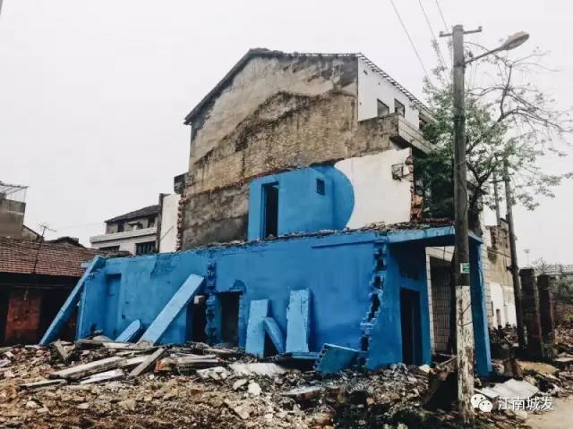 △ 這棟建筑是臨江最近的半拆遷建筑物的遺留，沅江和堤壩成為了展覽的天然背景。創(chuàng)作團(tuán)隊(duì)對(duì)這棟建筑進(jìn)行了半涂裝，將符號(hào)性的沅水曲線與拆遷進(jìn)行中的建筑立面進(jìn)行意義的疊造，它們共同觸發(fā)了場(chǎng)所空間多元語(yǔ)境的生成，把拆遷這種暫時(shí)破壞性、干擾性的介入行動(dòng)與沅水右岸發(fā)展的未來(lái)性、美好性緊密融合。